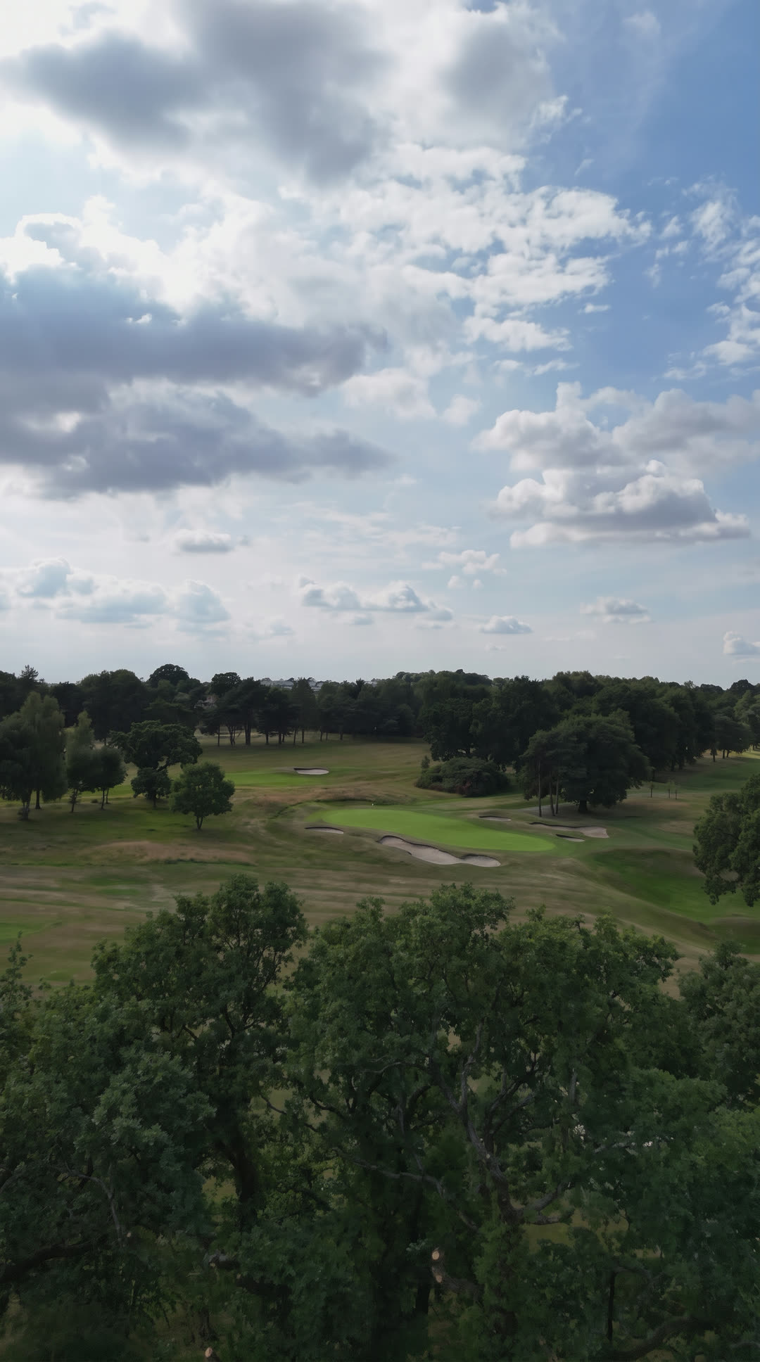 Parkland golf course under a summer sky, seen from above the trees