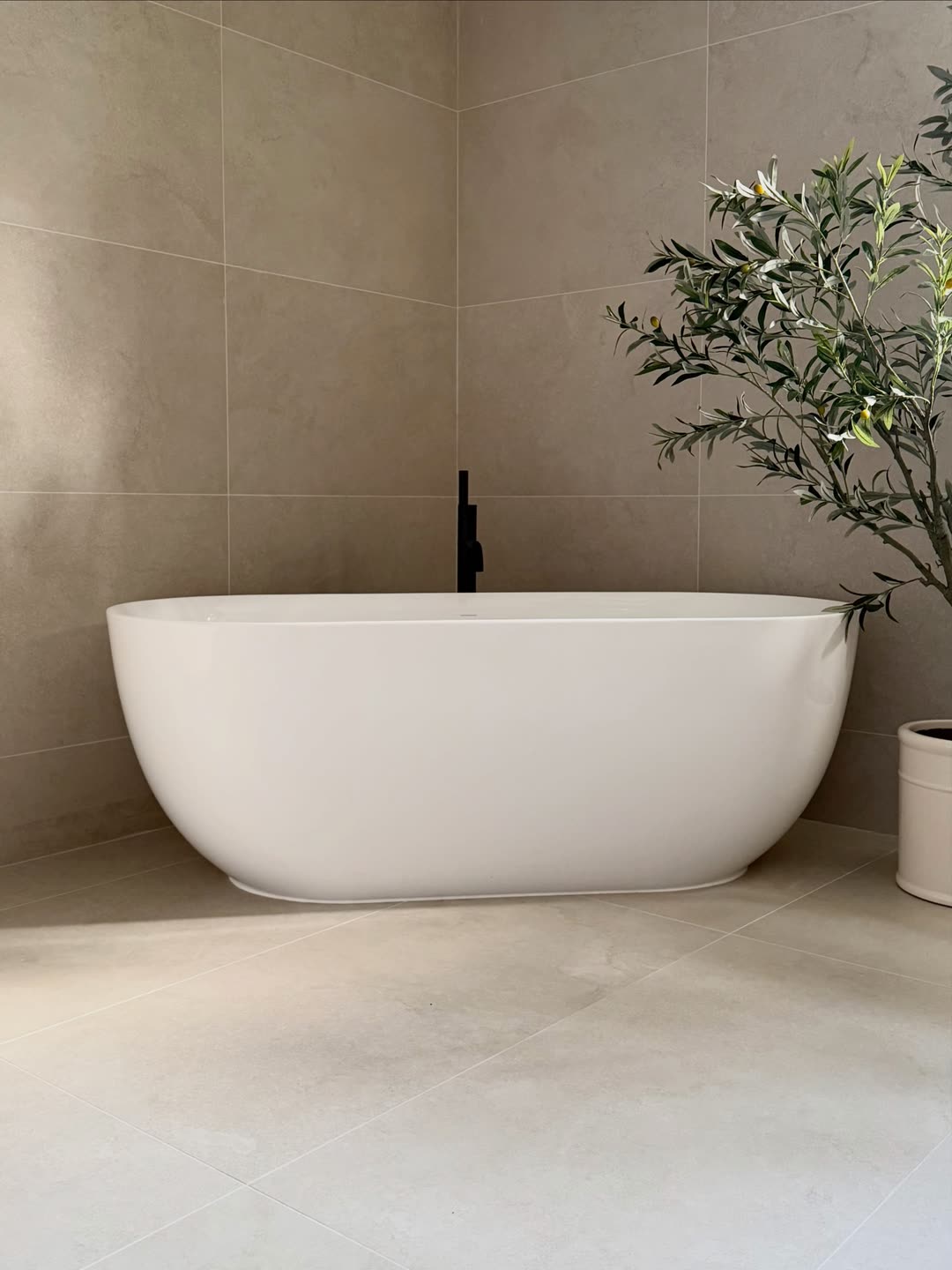 Freestanding bath and black tap beside an olive tree