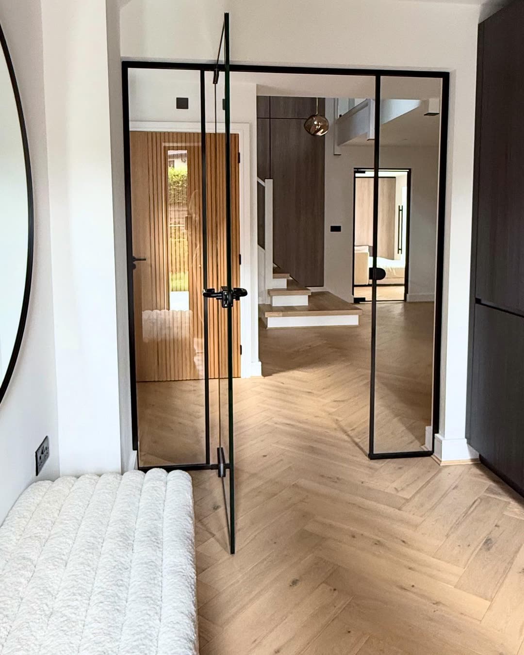 Entrance hall seen through black-framed glazed doors, herringbone oak underfoot