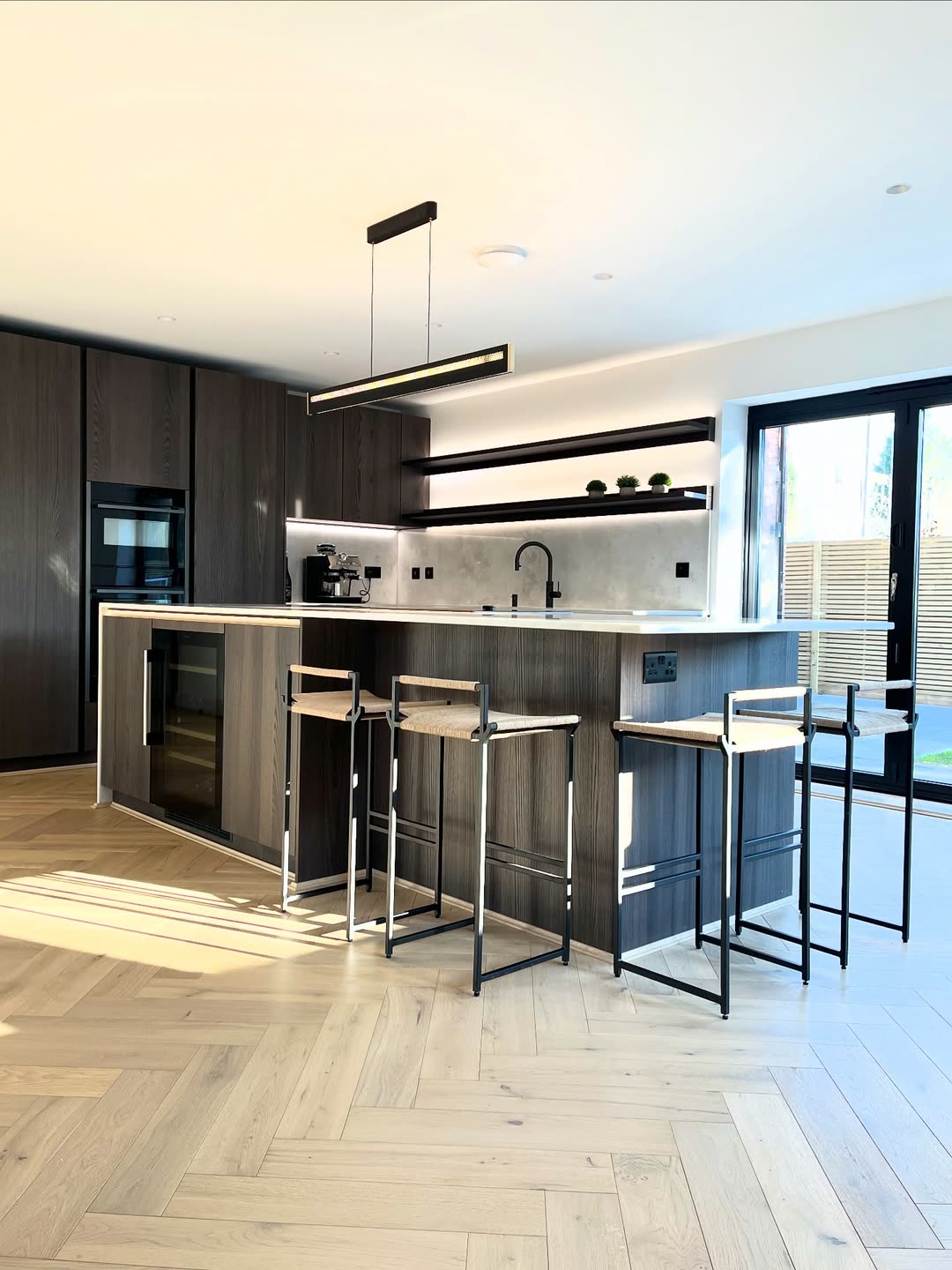 Handleless dark oak kitchen with a long island, linear pendant and lit shelving