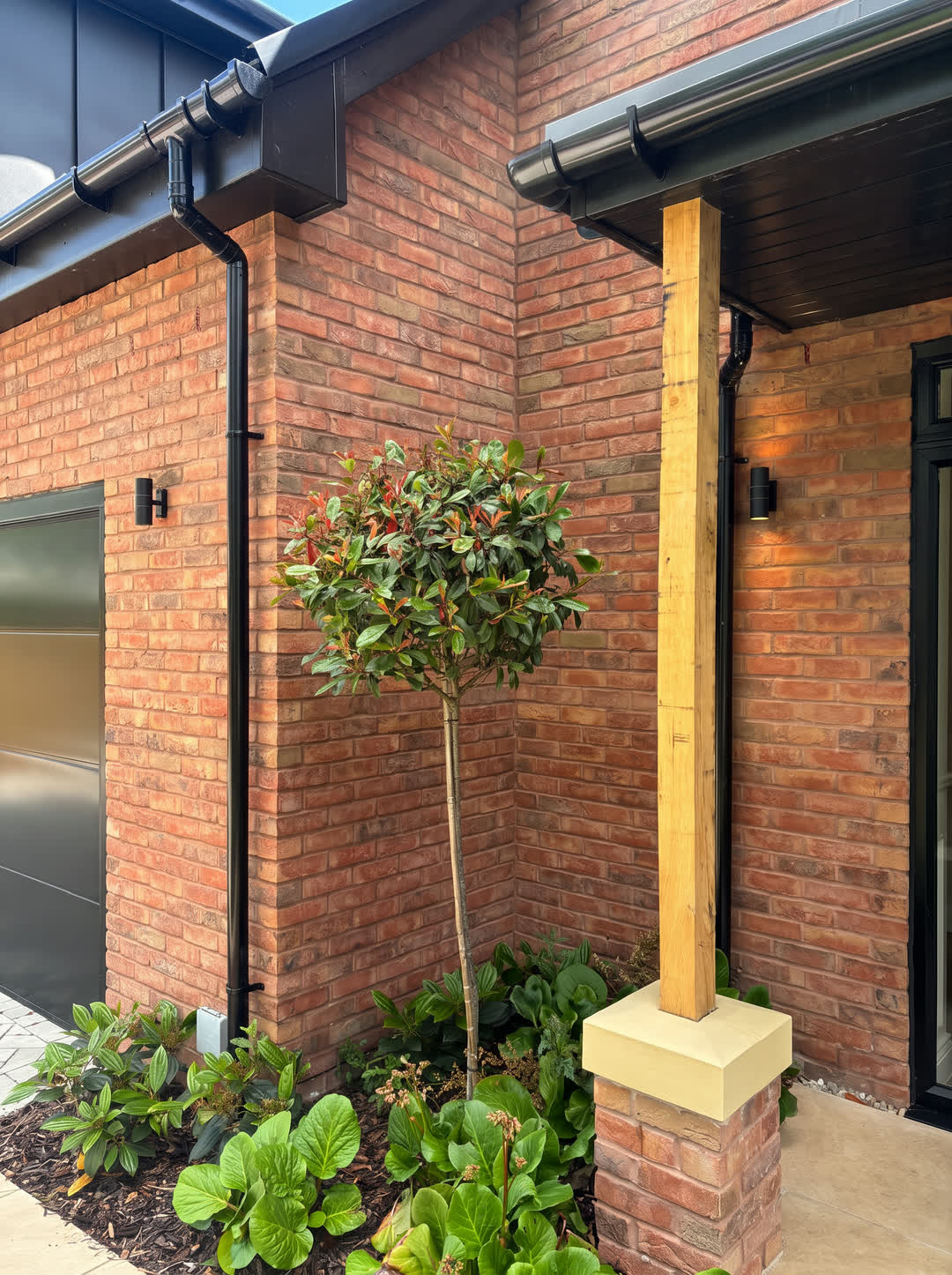 Oak porch post and standard photinia against the red brick, wall lights either side