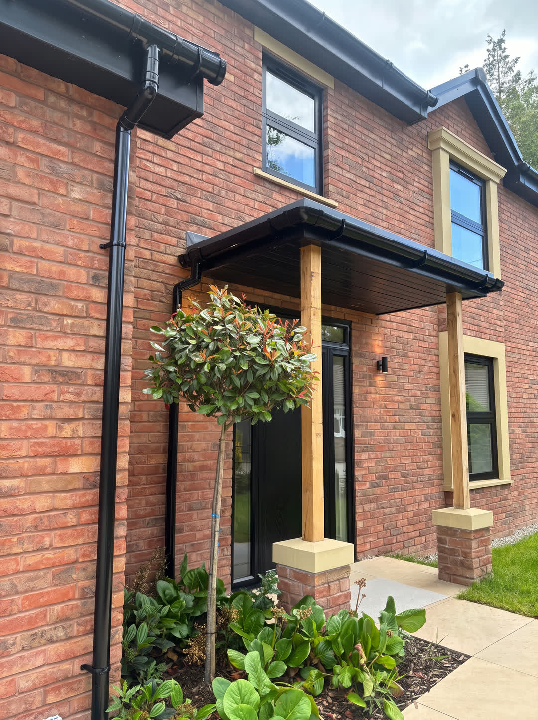 Oak porch on stone-capped brick piers at the front door, beside a standard photinia